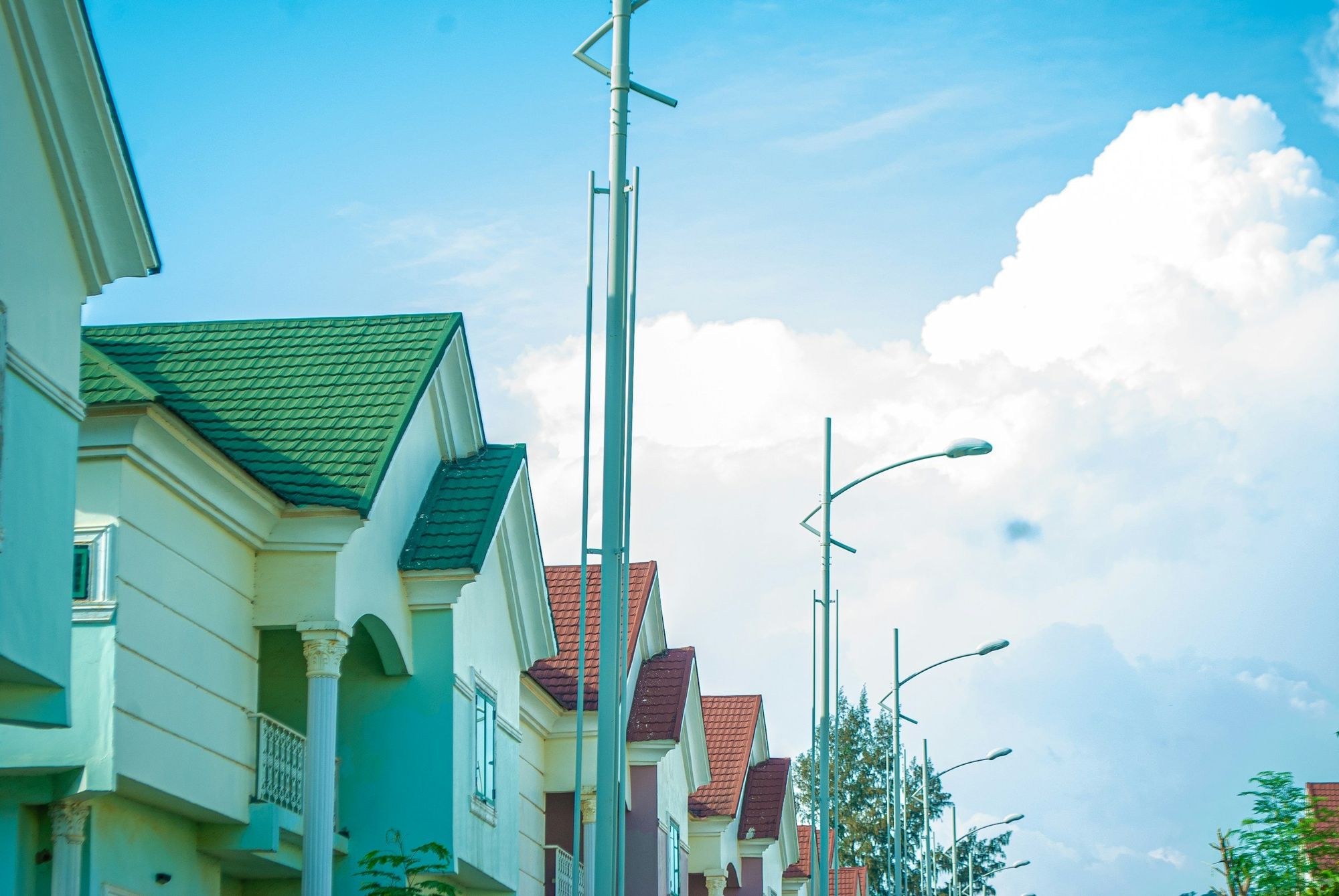 A row of estate homes with green tiled roofs and street lights under a bright sky.