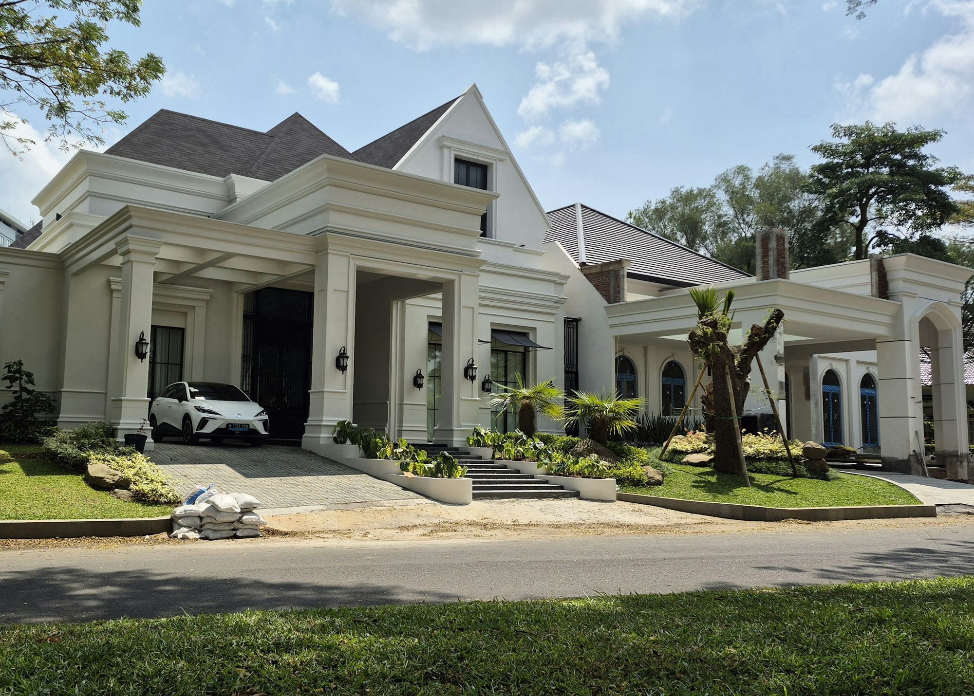 A large modern white home with a landscaped front garden on a newly paved estate road.