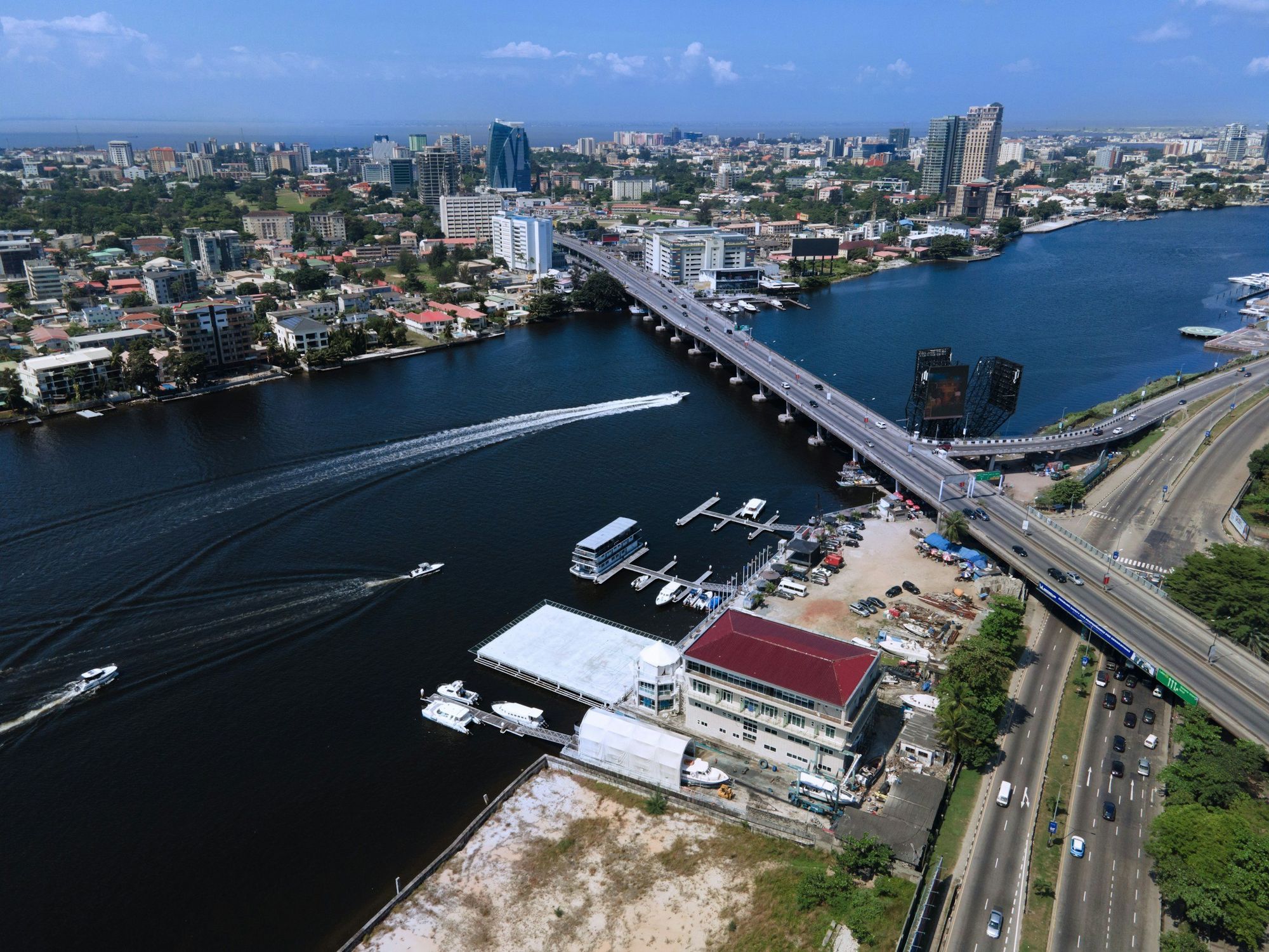 Aerial view of a modern Lagos waterfront: the lagoon, a bridge, boats and the city beyond.